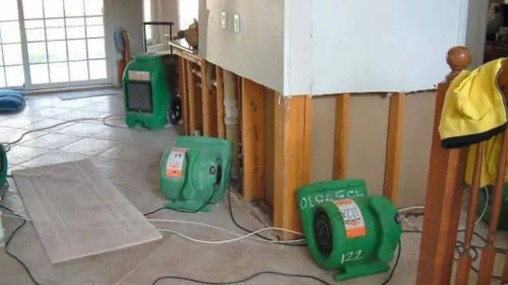 Green air movers placed along an opened wall in a room