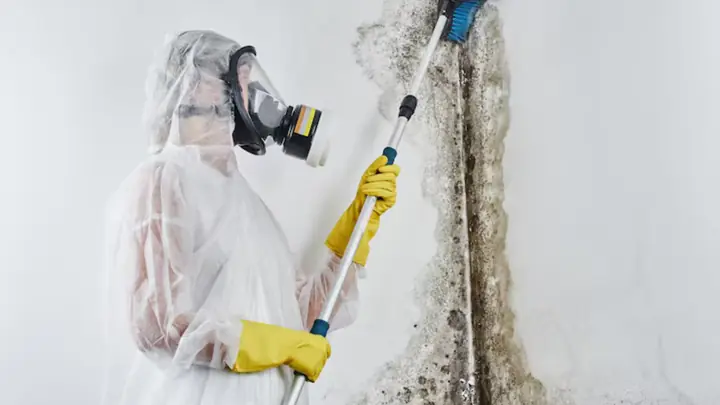 Worker in a respirator and protective suit treating a wall